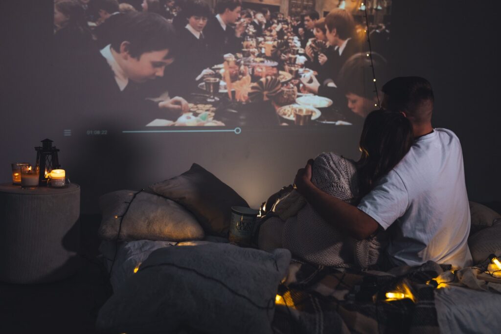 Couple relaxing on a bed with warm string lights, while a dinner video plays on the wall