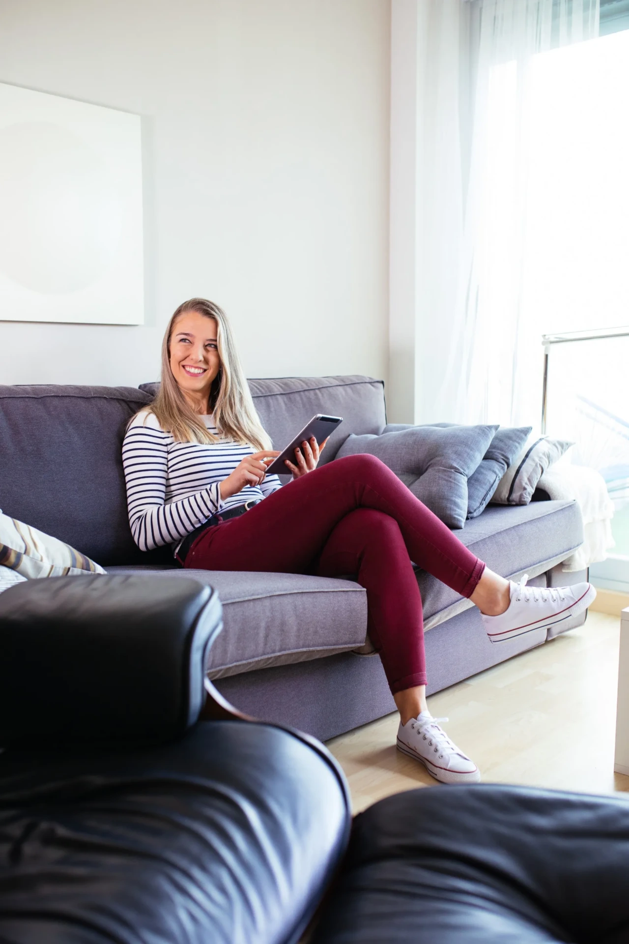 Woman sitting on a living room couch using a smartphone in a bright apartment interior
