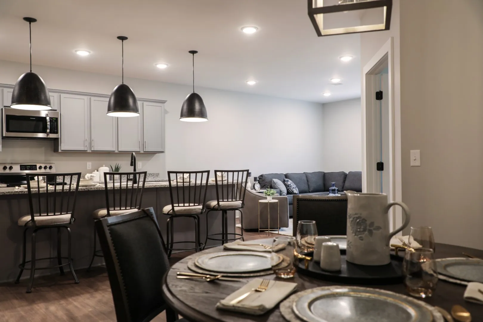 Bright modern kitchen and dining area with dark chairs and pendant lights, opening to a living room