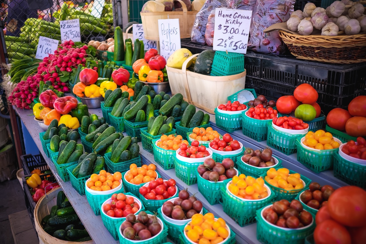 Farmers market produce display with baskets of colorful vegetables and handwritten price signs