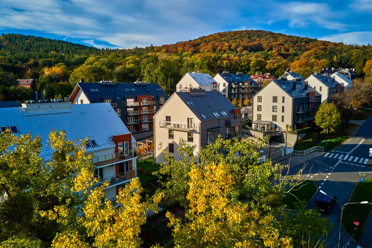 Aerial view of apartment buildings with balconies and blue roofs surrounded by autumn trees