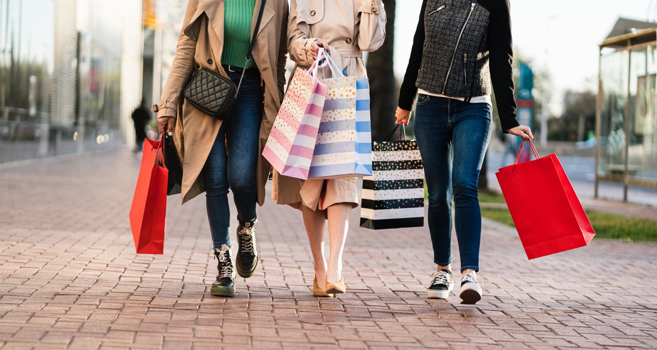 People walking outdoors carrying colorful shopping bags on a brick sidewalk